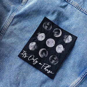 以下が含まれることがあります： 白い月のデザインと「It's Only a Phase」というテキストが刺繍された黒いパッチ