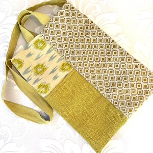 May include: A handmade tote bag with a shoulder strap. The bag features a patchwork design with various fabrics in shades of olive green, cream, and gold. The main body has a geometric pattern, while other sections have floral and textured designs.