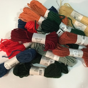 May include: A collection of 14 skeins of embroidery floss in various colors, including red, green, blue, orange, and beige. The skeins are labeled "Appleton Bros. Ltd. London".