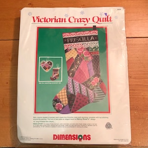 May include: A needlepoint kit package titled Victorian Crazy Quilt featuring a Christmas stocking with a patchwork design, floral patterns, and the name Priscilla embroidered on the cuff. The finished size is listed as 16 inches long.