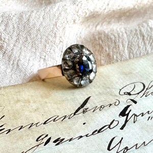 May include: A vintage ring with a blue sapphire surrounded by a halo of small diamonds. The ring is set in gold and has a delicate band.