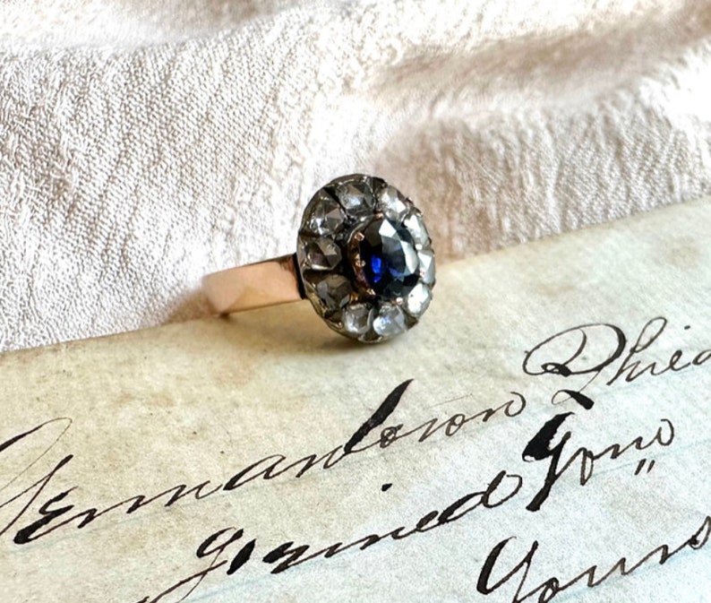 May include: A vintage ring with a blue sapphire surrounded by a halo of small diamonds. The ring is set in gold and has a delicate band.
