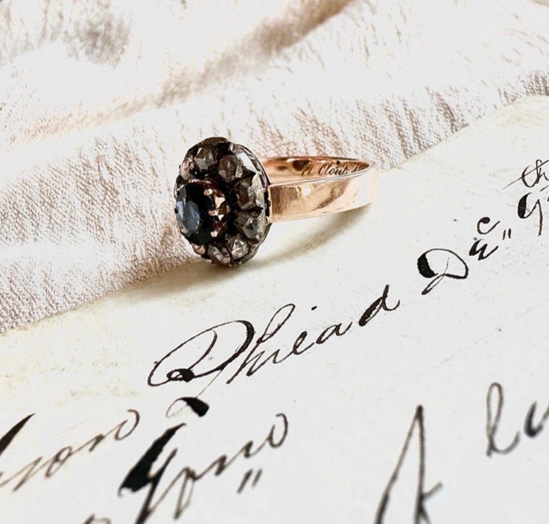 May include: A vintage ring with a black gemstone surrounded by a halo of small diamonds set in a gold band.