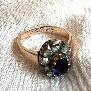 May include: A gold ring with a blue sapphire surrounded by diamonds. The inside of the band is engraved with "11 Oct 1887".