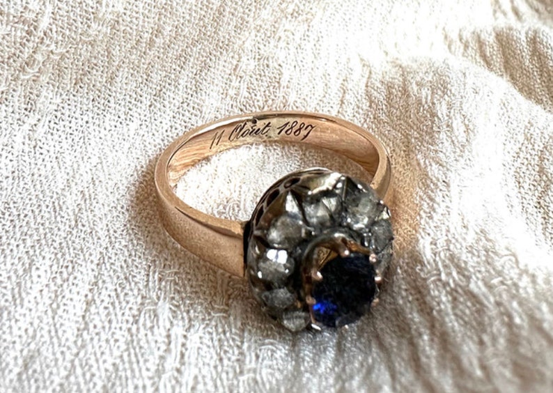 May include: A gold ring with a blue sapphire surrounded by diamonds. The inside of the band is engraved with "11 Oct 1887".