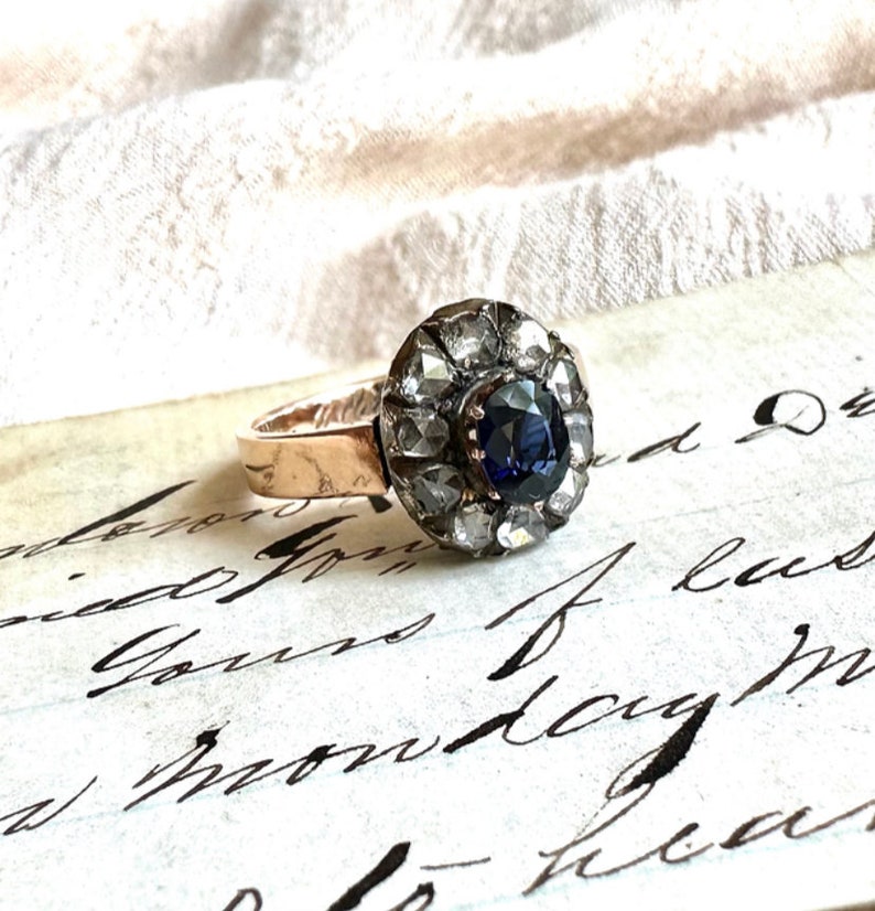 May include: A vintage ring with a dark blue sapphire surrounded by a halo of small diamonds. The ring is set in gold and has a delicate band.