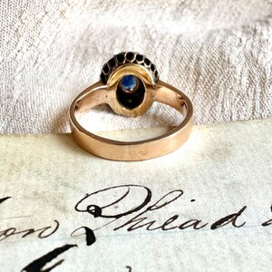May include: A gold ring with a blue gemstone surrounded by black stones. The ring is on a piece of paper with the words "Philad" written on it.