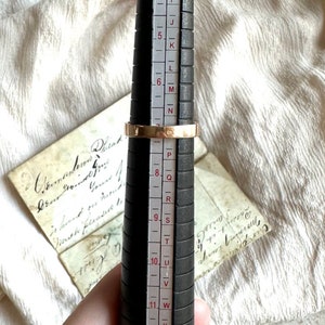May include: A gold ring with a band that is slightly wider than the average ring. The ring is being sized on a ring sizer that shows the ring is a size 8.