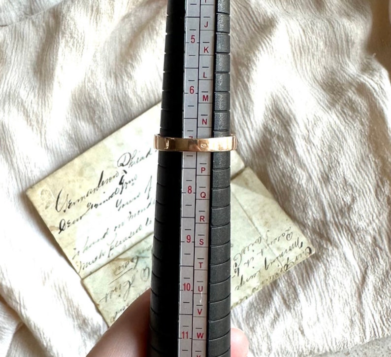 May include: A gold ring with a band that is slightly wider than the average ring. The ring is being sized on a ring sizer that shows the ring is a size 8.