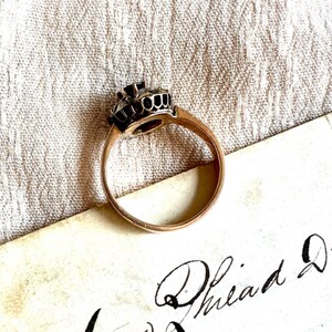 May include: A gold ring with a black stone set in a crown-like design. The ring is on a piece of paper with cursive writing.