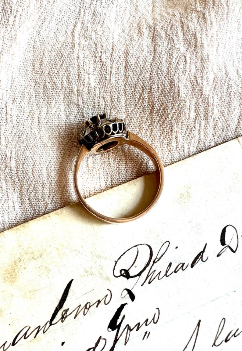 May include: A gold ring with a black stone set in a crown-like design. The ring is on a piece of paper with cursive writing.