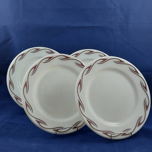 May include: Four white ceramic plates with a decorative maroon flame-like pattern around the rim. The plates are displayed on a blue background, suggesting a dining or kitchenware theme.