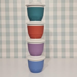 May include: Four colorful plastic containers stacked on top of each other. The containers are teal, red, purple, and blue, each with a white lid. The containers have a ridged texture and are designed for food storage.
