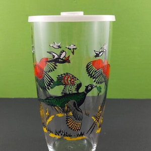 May include: A clear glass drinking glass with a white lid. The glass has a colorful design of pheasants flying in a field.