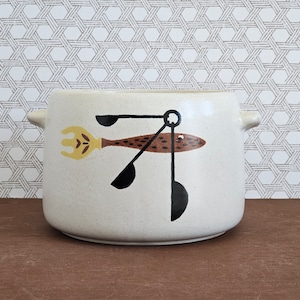 May include: A white ceramic soup tureen with a brown and yellow fish design. The fish has a fork and spoon attached to it.