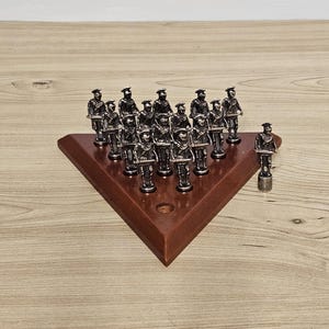 May include: A vintage chess set with silver soldier figurines on a triangular, dark brown wooden board. One soldier piece stands separately. The chess pieces are detailed and uniform in design. The board is approximately 20 cm across.