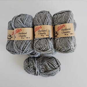 May include: Four skeins of grey Shetland Chunky yarn. Each skein has a brown paper label that reads "Zellers Shetland Chunky" with a small illustration and the weight of 50 g and 60 m. The yarn is a light grey colour.