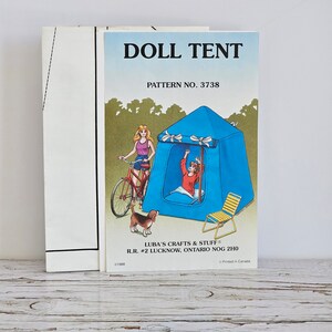 May include: A vintage sewing pattern for a doll's tent. The pattern is illustrated with a doll in a blue tent, a doll riding a bicycle, and a dog. The pattern number is 3738. The pattern is from Luba's Crafts & Stuff, RR #2 Lucknow, Ontario NOG 2H0.