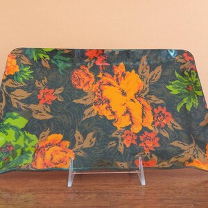 May include: Rectangular decorative tray with a floral pattern. The tray features large orange and yellow flowers with red accents on a dark green background. The tray is displayed on a clear plastic stand.