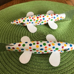 Puede incluir: Dos peces de madera blancos con lunares coloridos pintados sobre ellos. Los peces tienen aletas blancas y colas plateadas.