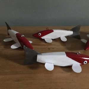 May include: Three wooden fishing lures painted in white and red with black eyes. The lures have a fin on the tail and two fins on the belly.