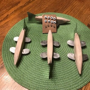 May include: Four wooden fish lures with silver fins and black eyes. The lures are arranged on a green circular placemat. A small cardboard sheet with white eyes and hooks is in the center.