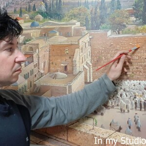 May include: A large oil painting depicting the Western Wall in Jerusalem with a crowd of people wearing white prayer shawls. The artwork features detailed stone textures, architectural structures, and a landscape background. Text reads: In my Studio in Jerusalem.
