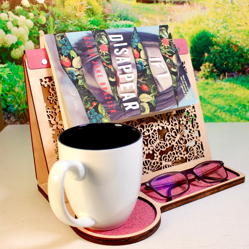 May include: A wooden book stand with a decorative butterfly design, holding a book titled "If I Disappear" by  Ellie Jane Brazier. A white mug and glasses are also on the stand.