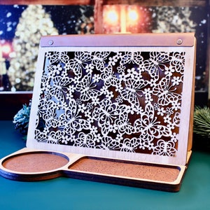 May include: A wooden phone stand with a decorative cutout design of butterflies and flowers. The stand has a small tray on the bottom for holding keys or other small items.