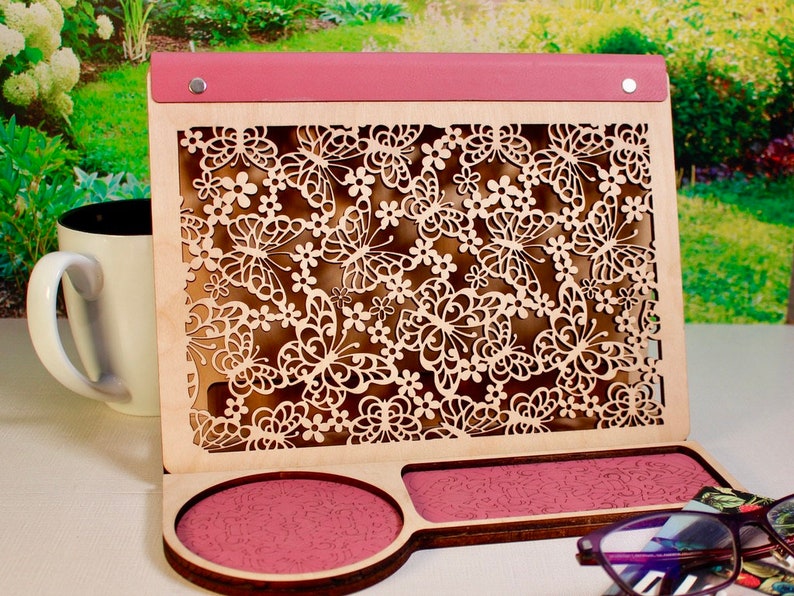 May include: A wooden organizer with a pink top and a cutout design of butterflies and flowers. The organizer has two compartments, one with a pink circle and the other with a pink rectangle.