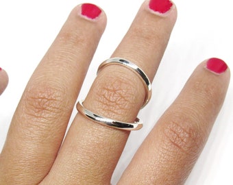May include: A silver ring with a double band design. The ring is worn on the middle finger of a hand with red nail polish.