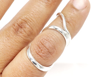 May include: A silver ring with a unique, twisted design. The ring is worn on the middle finger of a hand.