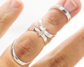 May include: A silver ring with a unique design that wraps around the finger. The ring is made of two bands that are intertwined and connected by a small loop.