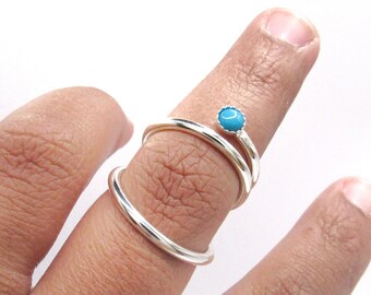 May include: Two silver rings, one with a turquoise stone, worn on a finger.