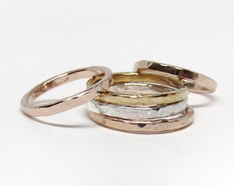 May include: A set of four stacking rings in different metals. The rings are all hammered and have a textured finish. The rings are in shades of gold, silver, and rose gold.