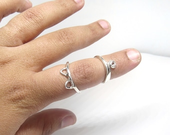 May include: Two silver rings on a finger. One ring is a simple band with a small round stone. The other ring is a delicate design with two heart shapes.