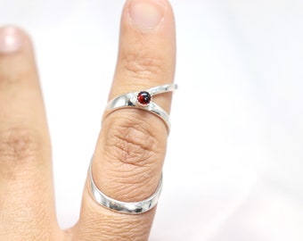 Op de afbeelding: Een zilveren ring met een rode edelsteen in het midden. De ring is ontworpen om om de vinger te wikkelen.
