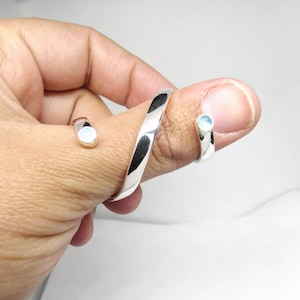 May include: A silver thumb ring with two white opalescent stones set into the band. The ring is twisted and has a unique design.