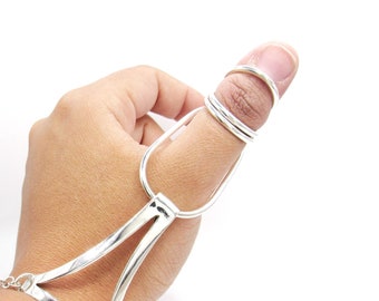 May include: A silver-toned hand chain with a thumb ring and finger loop. The jewelry features a geometric design with a triangular element connected to a chain bracelet. The thumb ring has two bands.