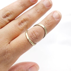 May include: Two gold-colored rings are worn on a finger. The rings are simple bands, and the finger is against a white background. The rings are made of a metal with a slightly textured surface.