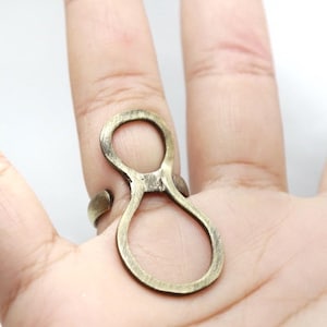 May include: A bronze-colored ring with an abstract figure-eight design. The ring is worn on a finger, showcasing its open, looping shape. The metal has a slightly aged appearance, adding to its unique aesthetic.