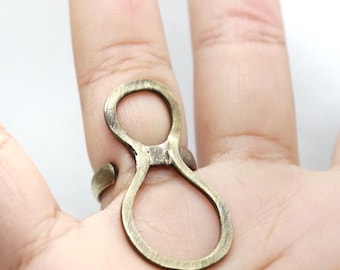 May include: A bronze-colored ring with an abstract figure-eight design. The ring is worn on a finger, showcasing its open, looping shape. The metal has a slightly aged appearance, adding to its unique aesthetic.