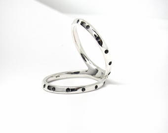May include: Two silver rings with black dots around the band. The rings are interlocked and are designed to be worn on two fingers.