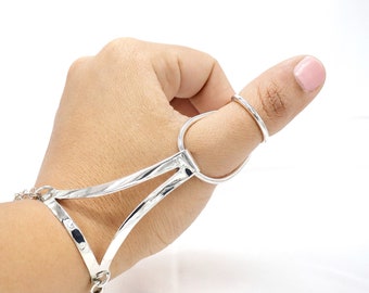 May include: Silver thumb ring with a geometric design. The ring is connected to a silver bracelet with a chain detail.