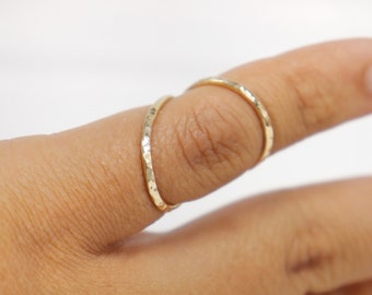 May include: Two thin gold rings with a hammered texture, worn on a finger.