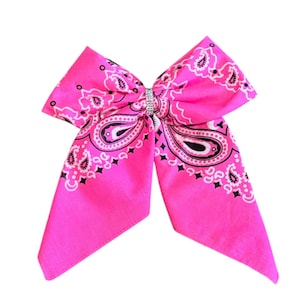 May include: A vibrant pink bandana bow featuring a paisley design in black and white. The bow is adorned with a silver rhinestone centrepiece. This is a hair accessory.