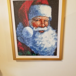 Peut inclure: Une peinture de diamant encadrée représentant le Père Noël avec un chapeau rouge et une barbe blanche. L'arrière-plan est bleu foncé avec des étoiles blanches.