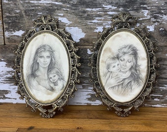 May include: Two oval framed pencil drawings of mothers and children. The frames are ornate and gold colored. The drawings are on a cream colored background.