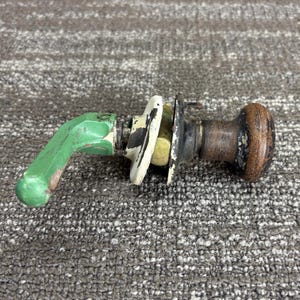 May include: An antique door handle with a green lever, white and black accents, and a brown knob. The handle shows signs of wear, suggesting it is a vintage item. The hardware is likely made of metal.