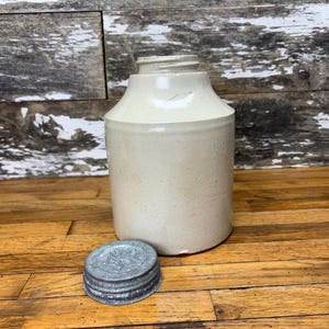 May include: A vintage white ceramic jar with a metal lid. The jar has a slightly textured surface and is in good condition.